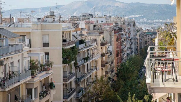 Una zona urbana densamente poblada con edificios de varios pisos, balcones y un paisaje montañoso de fondo.