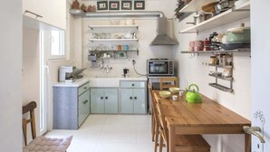 Cocina compacta con una mesa de madera, un microondas y diversos utensilios de cocina en estantes.