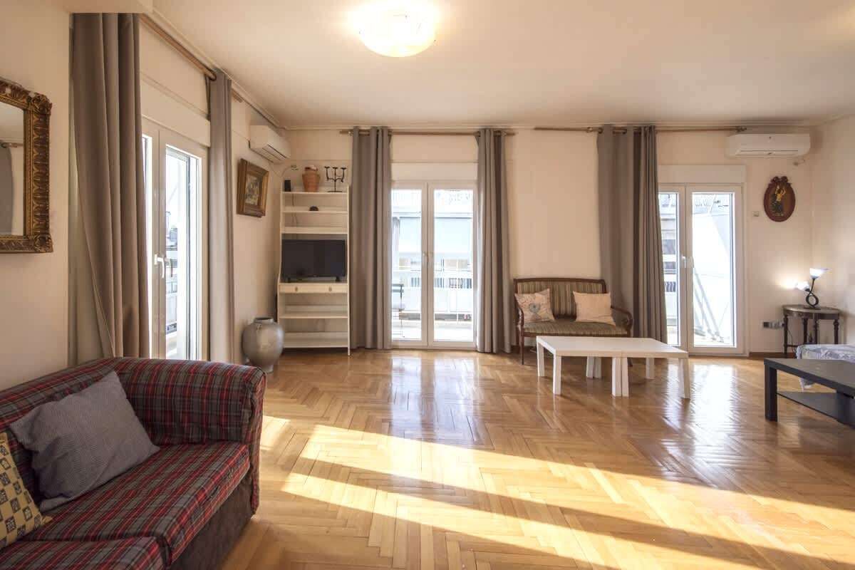 Ein geräumiges Wohnzimmer mit Holzboden, einer Couch, einem Couchtisch und einem Fernseher.