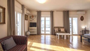 Amplio salón con piso de madera, un sofá, una mesa de centro y un televisor.