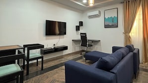 Un salon moderne avec un canapé, des fauteuils, un téléviseur et un bureau.