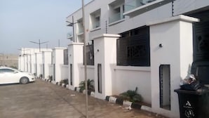 Une rangée de bâtiments modernes, blancs, dotés de balcons, et une voiture blanche garée devant.