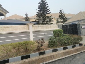 Una calle residencial con entrada protegida por una reja, un camino de acceso y una hilera de casas de estilo arquitectónico similar.