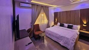 Une chambre d’hôtel moderne avec un grand lit, un bureau et une chaise. Il y a un téléviseur accroché au mur et une fenêtre avec des rideaux.