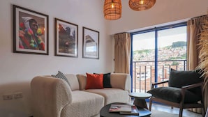 Un salon moderne avec un canapé beige, une table basse ronde et une vue sur le paysage urbain, visible à travers de grandes fenêtres.