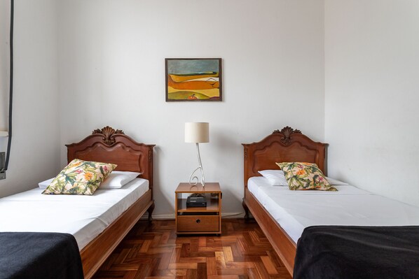 A room with two wooden beds, each with floral pillows, a nightstand with a lamp, and a painting on the wall.