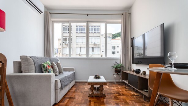 Una sala de estar moderna con sofá, mesa de centro y zona de comedor, con televisor y una copa de vino.