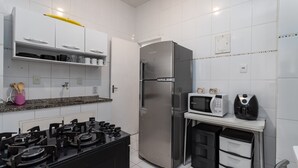 Una cocina moderna con armarios blancos, un refrigerador de acero inoxidable, una estufa a gas, un microondas y una cafetera.
