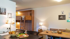 Un comedor con una mesa de madera, sillas, una mesa de buffet con comida y un armario de madera con una escalera.