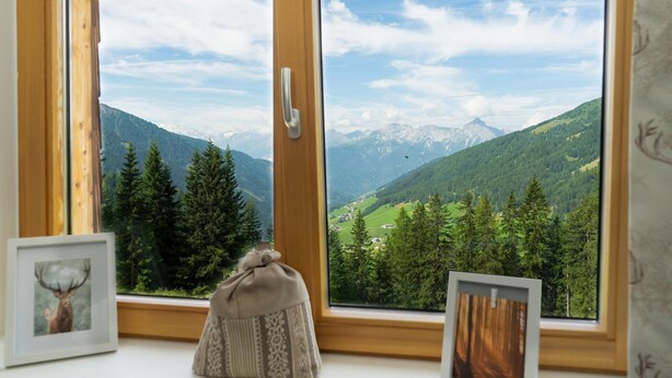 Ventana con vistas a un paisaje montañoso, enmarcada por un marco de madera y un tirador.