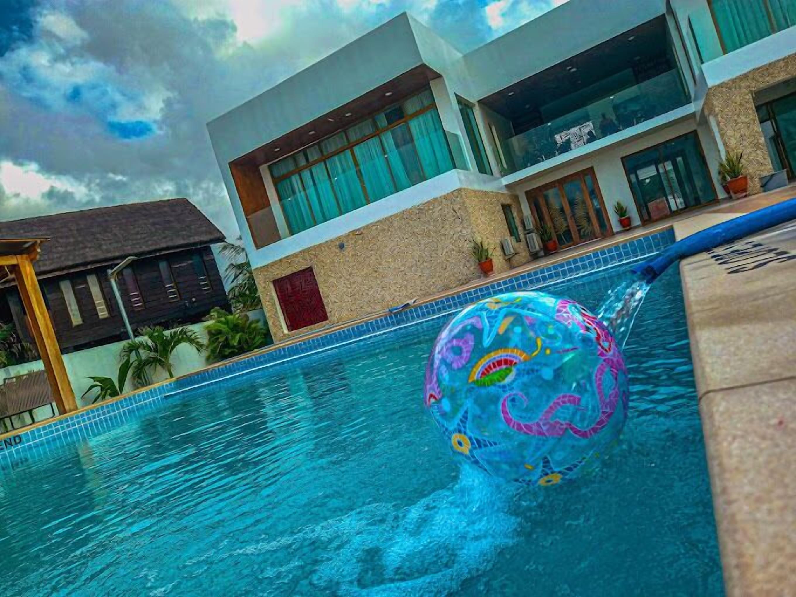 A swimming pool with a colorful inflatable ball, a modern building with large windows, and a tropical setting with palm trees.