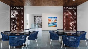 A modern dining area with round tables and blue chairs, wooden ceiling, and abstract art on the walls. - Pura Vida Beach (Lagos)