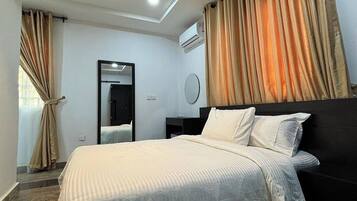 A modern hotel room with a large bed, a round mirror, and beige curtains.