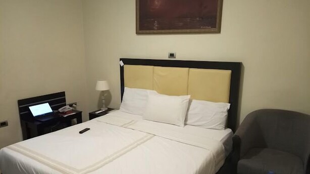 A hotel room with a bed, a desk with a laptop, a chair, and a small table with a water bottle. - Pura Vida Beach (Lagos)