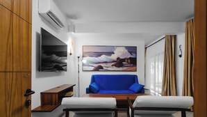 A modern living room with a blue sofa, white armchairs, a flat-screen TV, and a painting of a seascape. - Pura Vida Beach (Lagos)