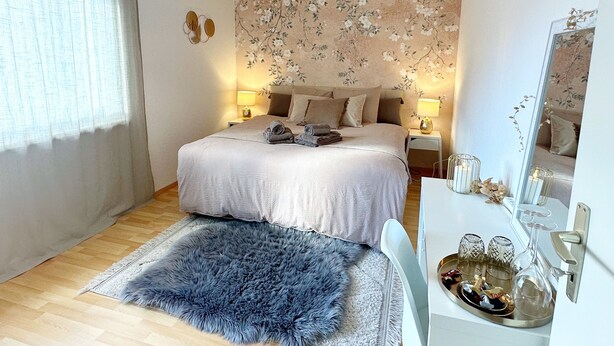 A neatly arranged bedroom with a large bed, a fluffy rug, bedside lamps, and a mirror. - Charming room in the heart of the Alps (Chamoson)