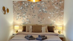 A bedroom with a floral wallpaper, a bed with two pillows, two bedside lamps, and two rolled towels on the bed. - Charming room in the heart of the Alps (Chamoson)