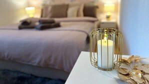 A neatly made bed with a white headboard, a bedside table with a candle in a gold wire holder, and a wall with a floral pattern. - Charming room in the heart of the Alps (Chamoson)