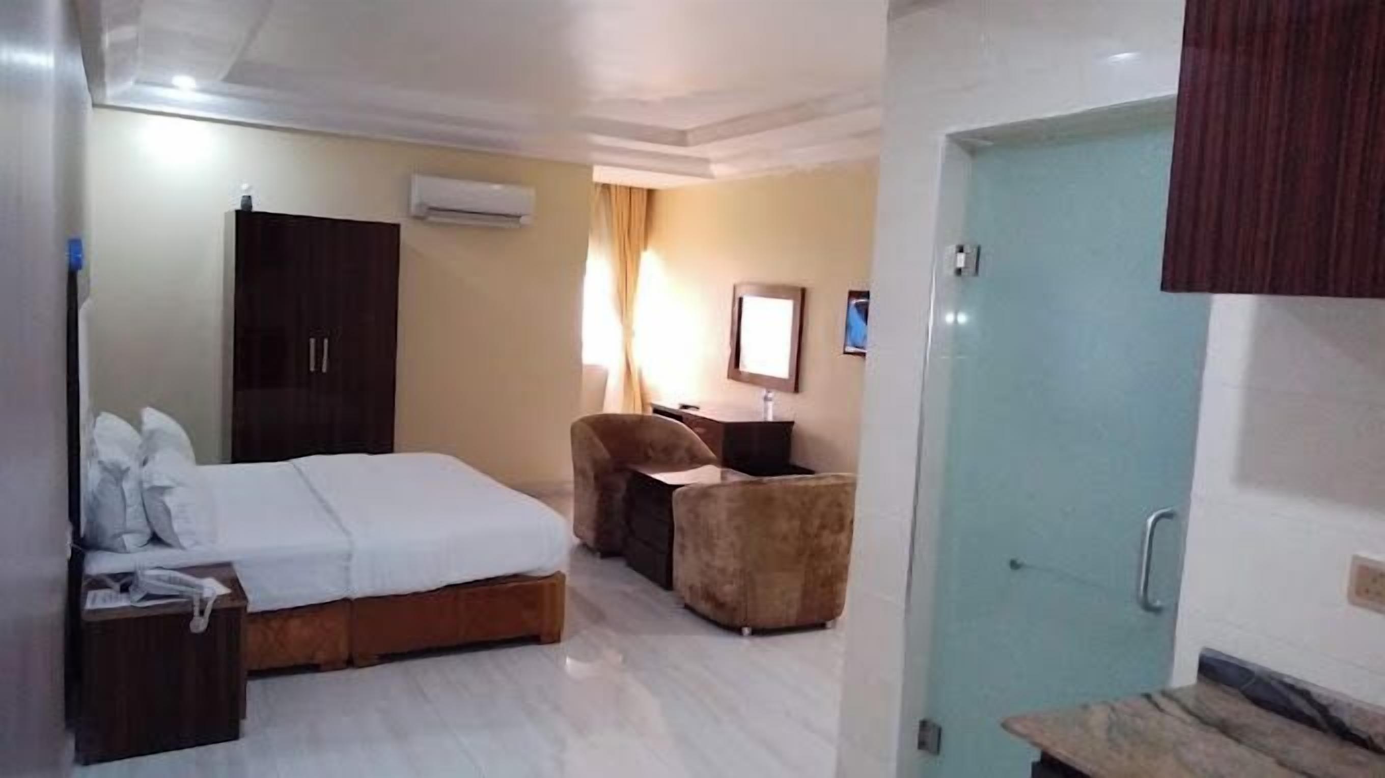 Habitación de hotel con cama, escritorio, silla, equipo de aire acondicionado y puerta.