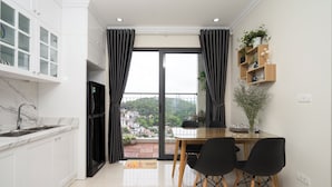 A modern kitchen with white cabinets, a black refrigerator, and a dining area with a wooden table and black chairs. - MonHomestay Ha Long-Amazing view balcony (Hong Gai)