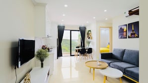 A modern living room with a flat-screen TV, a sofa, a coffee table, and a dining area with a table and chairs. - MonHomestay Ha Long-Amazing view balcony (Hong Gai)