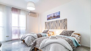 A hotel room with two beds, a cityscape painting, a textured wall hanging, and a large window with a view.