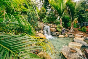 Une cascade au cœur d’un jardin luxuriant, agrémenté de rochers et de plantes tropicales.