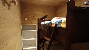 Et værelse i en træhytte med køjesenge, en stige og et hvidt reolsystem.