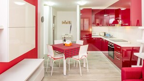 Une cuisine moderne avec des meubles de couleur rouge, une table à manger recouverte d’une nappe à carreaux rouges et noirs, et des chaises blanches.