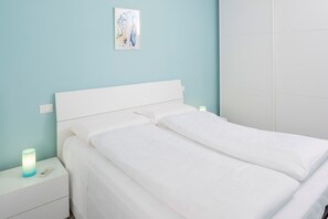 Ein ordentlich bezogenes Bett mit weißen Leinen in einem Zimmer mit hellblauen Wänden und einem weißen Nachttisch mit einer Lampe.