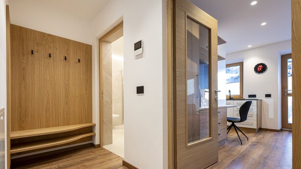 Un interior moderno con un banco de madera, una puerta corredera, un escritorio con una silla y un reloj en la pared.