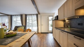 A modern kitchen with wooden cabinets, a black countertop, and a dining area with a wooden table and chairs. - 1002A Apartments No.7 Sella (Ortisei)