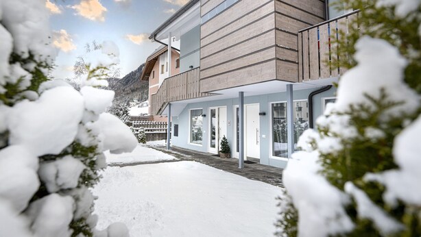 A modern building with a wooden facade and large windows, surrounded by snow-covered ground and trees. - 1002A Apartments No.7 Sella (Ortisei)