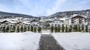 A snow-covered village with traditional chalet-style buildings, a paved pathway leading to a gate, and a mountainous backdrop. - 1002A Apartments No.7 Sella (Ortisei)