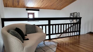 Ein gemütliches Wohnzimmer mit einem bequemen Sessel, einer Holzbalkendecke und einer Treppe mit Geländer.