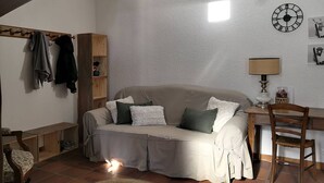 Ein gemütliches Wohnzimmer mit einer Couch, einem Holzstuhl, einem kleinen Tisch mit Lampe und einer Wanduhr.