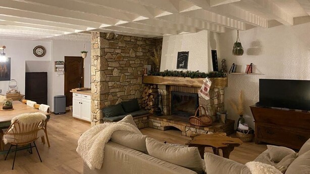 Ein gemütliches Wohnzimmer mit Kamin aus Stein, Holzbalkendecke, einer Couch und einem Fernseher.