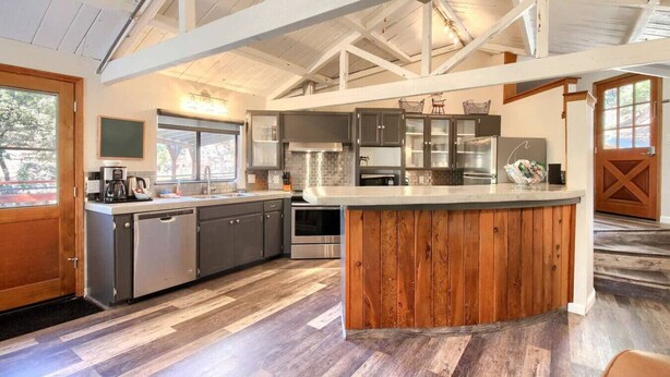 A modern kitchen with a central island, built-in appliances, and a high ceiling with exposed beams. - Waterfall House - Riverfront - BBQ - Sleeps 4 (Oakhurst)