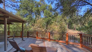 Une terrasse en bois, dotée de meubles en osier et d’une balustrade donnant sur une zone boisée.