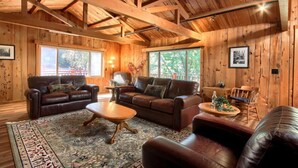 L’intérieur chaleureux d’un chalet avec des murs et un plafond en bois, deux canapés en cuir, une table basse et un tapis.