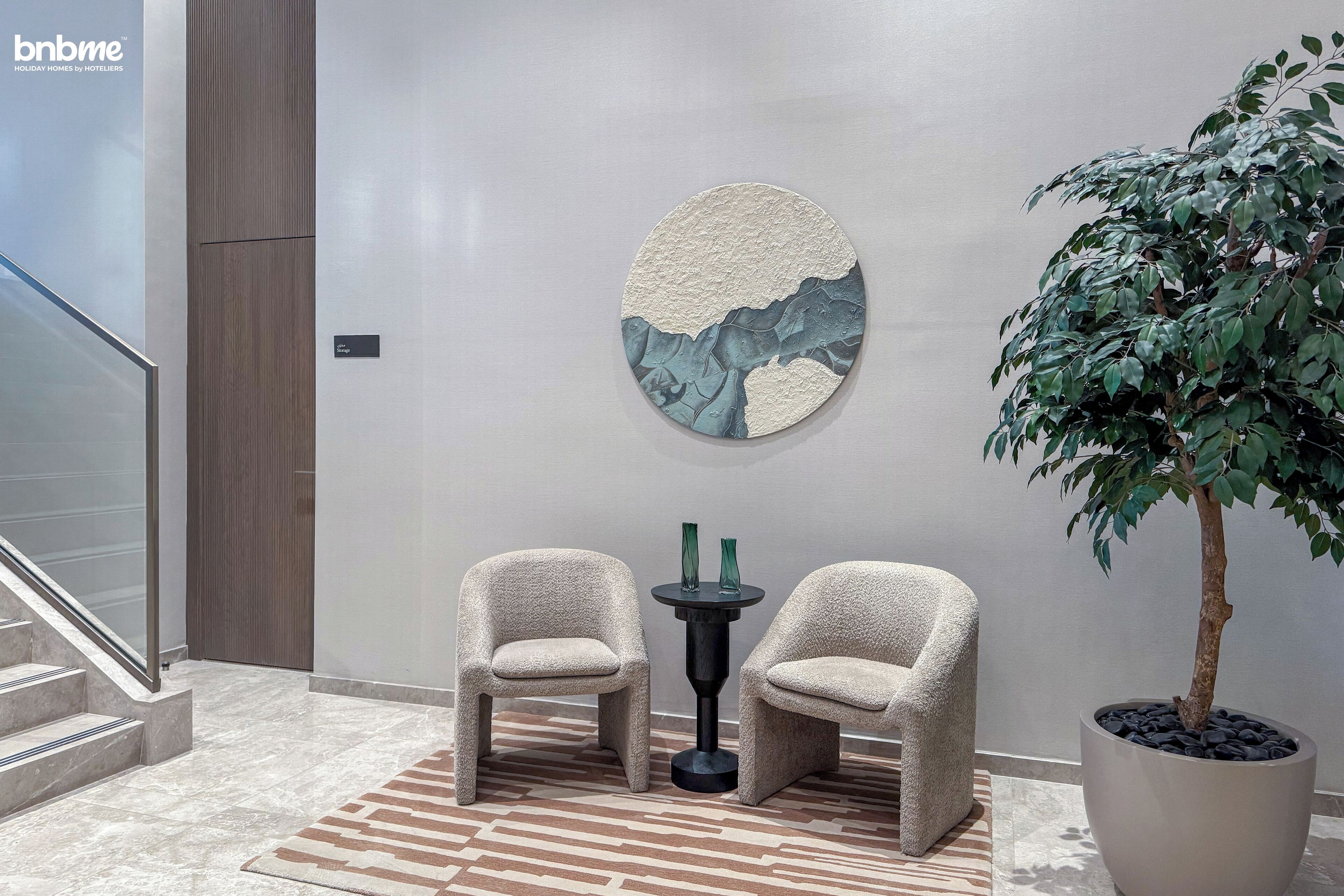 Een moderne lobby met twee comfortabele fauteuils, een ronde wanddecoratie, een potplant en een trap.