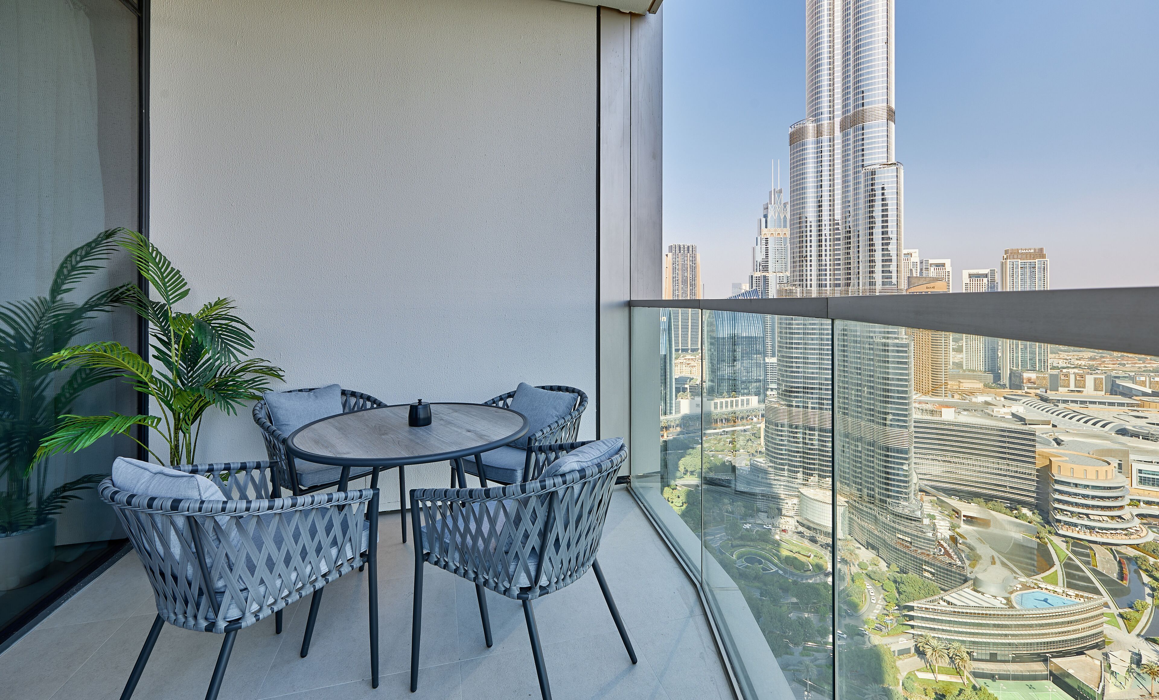 Un balcone con un tavolo rotondo e sedie, una pianta in vaso e vista su un panorama urbano con edifici alti.