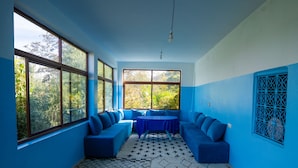 A room with a blue color scheme, large windows, a sofa, and a patterned rug. - Dar Assounfou (Aït Majden)