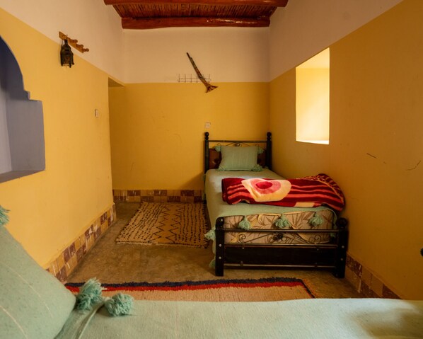 A small, cozy bedroom with a bed, a window, and a wooden ceiling. - Dar Assounfou (Aït Majden)