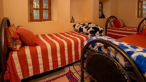 A room with two beds, each with a distinct patterned bedspread. There are windows with decorative glass panes, and the room has a wooden ceiling. - Dar Assounfou (Aït Majden)