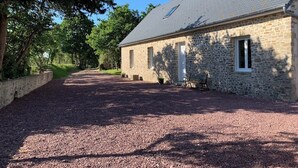 A stone building with a gravel driveway and a small bench. - Blackberry Cottage country cottage (Lessay)