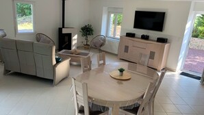 A modern living room with a round dining table, a sofa, a TV, and a fireplace. - Blackberry Cottage country cottage (Lessay)