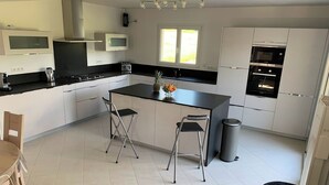 A modern kitchen with a central island, two bar stools, a microwave, and a built-in oven. - Blackberry Cottage country cottage (Lessay)