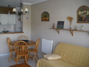 A dining area with a table and chairs, a radiator, and a sofa with a cushion. - Apartment Near Roses Beach With Pool (Roses)