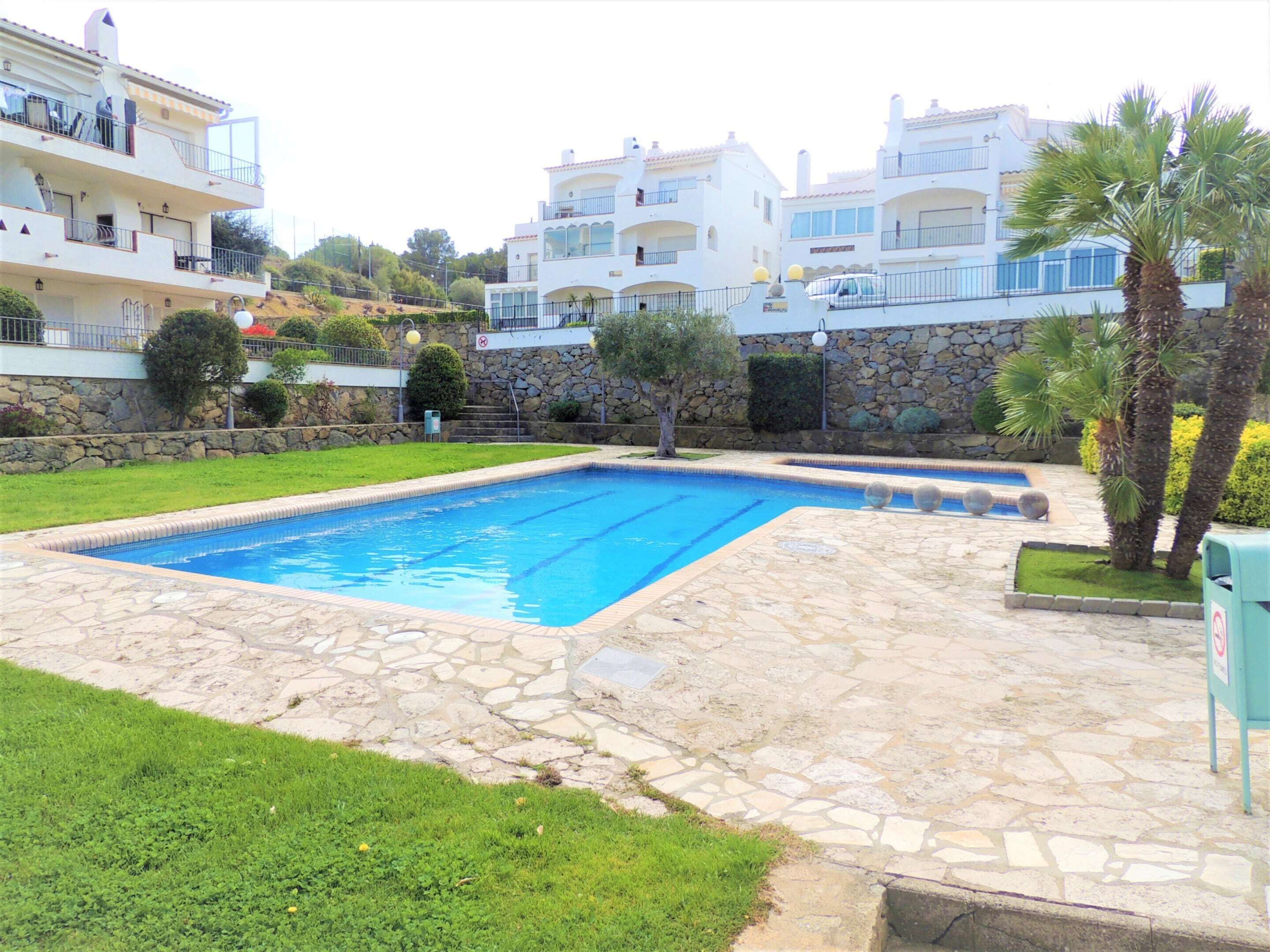 A swimming pool with stone tiles, surrounded by a grassy area and a stone wall.